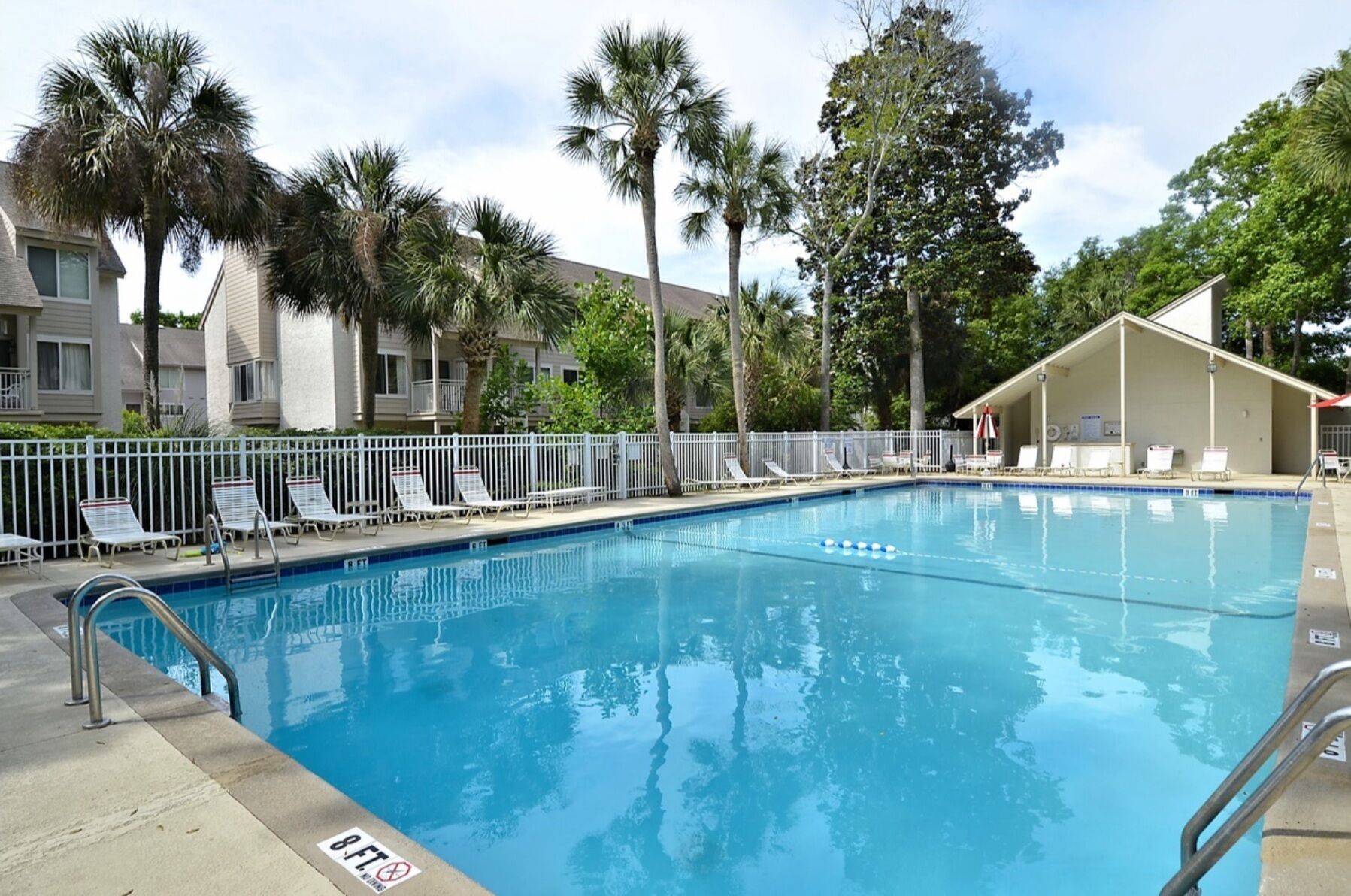A swimming pool with a 8-ft depth marker, surrounded by palm trees and a white fence.