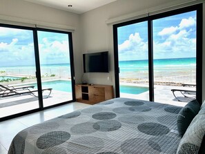 Een slaapkamer met een groot bed, een televisie en uitzicht op de oceaan.