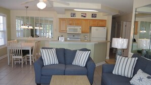 A modern living room with a gray sofa, wooden coffee table, and a dining area with a white table and chairs. - 2109 2 Bedroom Villa by RedAwning (Calabash)