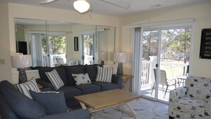 A living room with a sofa, armchairs, a coffee table, and a patterned armchair. There is a large mirror, a lamp, and a view of the outdoors through a sliding glass door. - 2109 2 Bedroom Villa by RedAwning (Calabash)