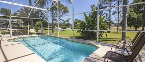 En swimmingpool med ett vitt poolområde, omgiven av solstolar och ett takförsett område med utsikt över det omgivande landskapet.