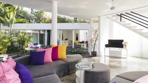 A modern living room with a curved grey sofa, glass coffee table, and a flat-screen TV. - Villa La Sirena 2 Minutes From Beach 3 Bedroom Villa by RedAwning (Seminyak)