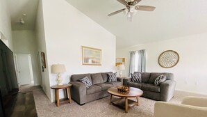 A living room with a grey sofa, a round coffee table, a TV, and a ceiling fan.