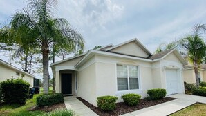 A single-story house with a front entrance, a garage, and a small front yard with trimmed bushes and a palm tree.