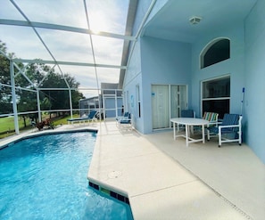 A swimming pool with a covered patio area, outdoor seating, and a view of the surrounding landscape.