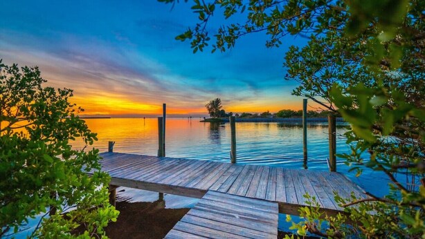 Muelles de madera que se adentran en aguas tranquilas con un atardecer de fondo.