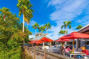An outdoor dining area with red umbrellas labeled 'TBBL', surrounded by palm trees and a wooden deck. - U409 SUN RISING- BALCONY WATERVIEW- SELF CHECK IN- PRIVATE BEACH RESORT (Ruskin)
