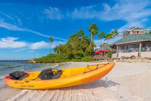 A beach with a yellow kayak, palm trees, and a building with a green roof. - U409 SUN RISING- BALCONY WATERVIEW- SELF CHECK IN- PRIVATE BEACH RESORT (Ruskin)