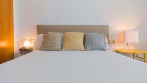 Un lit bien fait avec trois oreillers, une table de chevet avec une lampe et une petite table avec une lampe.