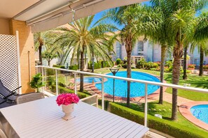 Un balcó amb vistes a una piscina envoltada de palmeres i un jardí ben cuidat.