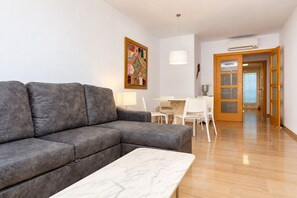 Un saló modern amb un sofà gris, una taula de centre de marbre, una taula de menjador amb caires i un quadre a la paret.