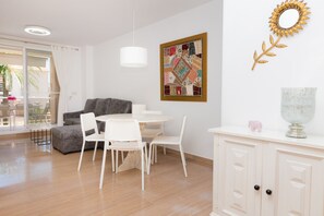 A modern living room with a grey sofa, white chairs, a round table, and a white cabinet with a decorative mirror and vase. - Golden Gardens Saudade Apartment Javea Arenal (Javea / Xàbia)