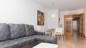 Un salon avec un canapé gris, une table basse blanche, un tableau au mur et une porte donnant sur une autre pièce.