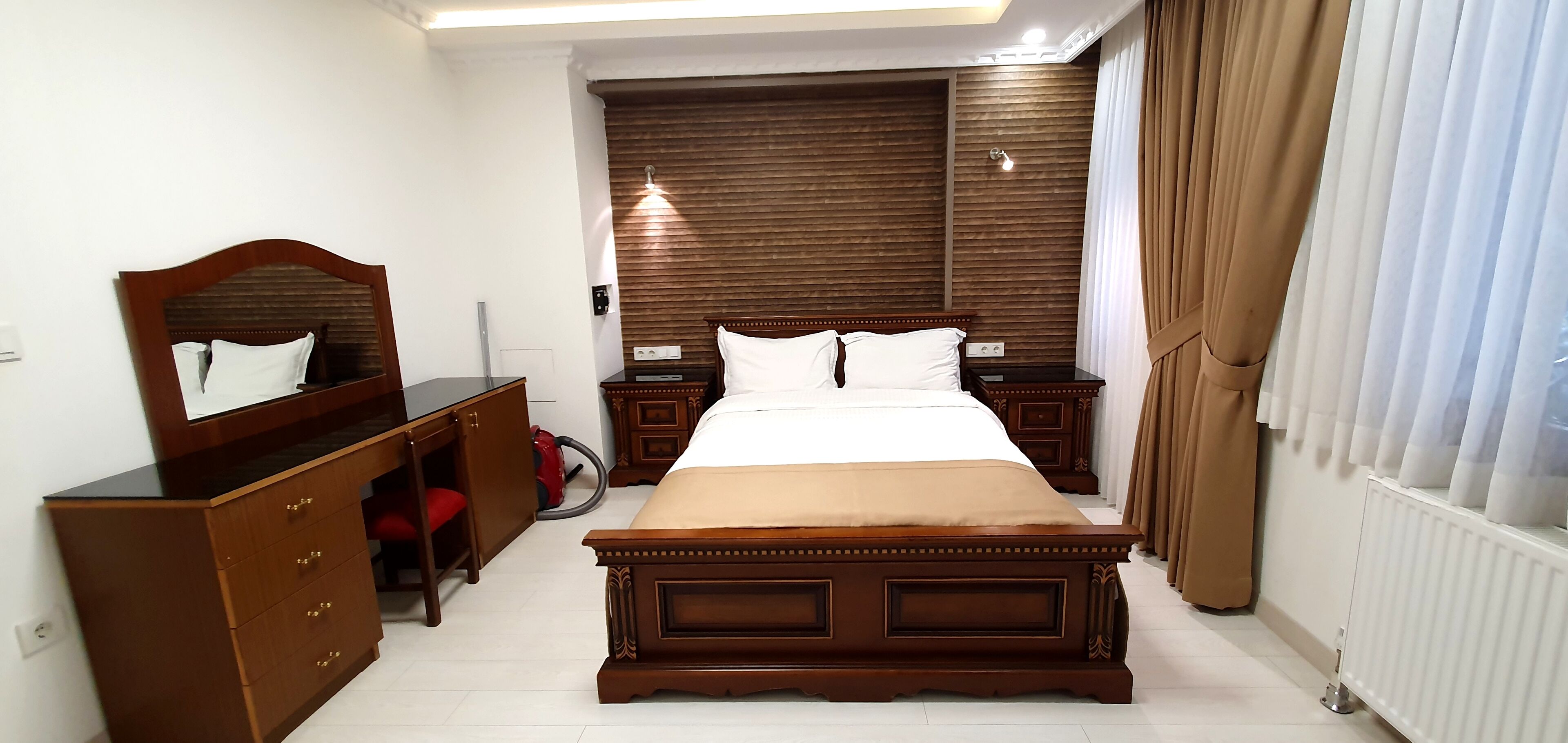 A bedroom with a large bed, wooden headboard, bedside tables, a dresser, and a mirror.