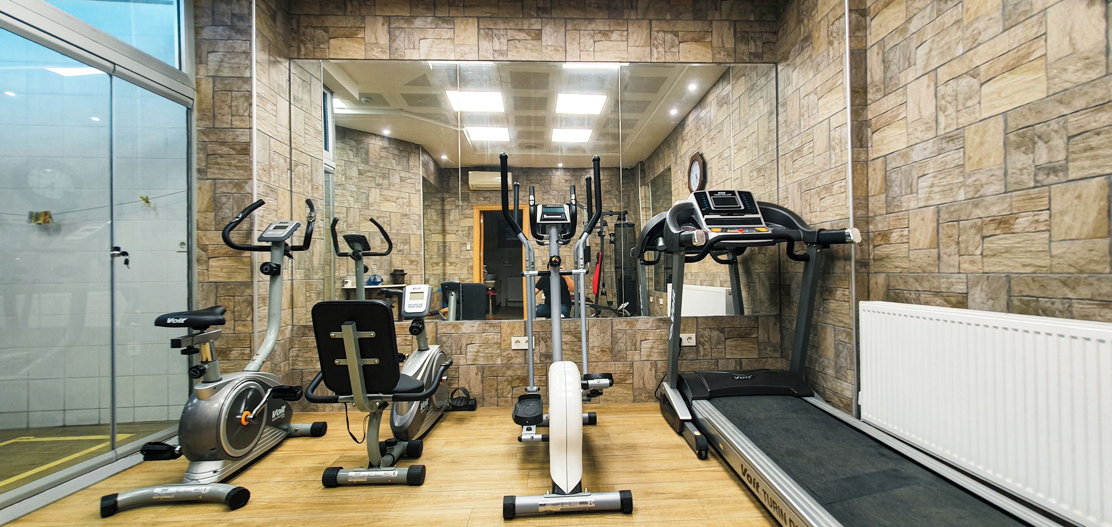Ein Fitnessstudio mit unterschiedlichen Trainingsgeräten, darunter Laufbänder, Ergometer und ein Rudergerät.
