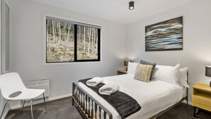 A bedroom with a bed, a window with a forest view, a painting, and a chair. - Central Queenstown Apt 15a - with Gym walk to town (Queenstown)