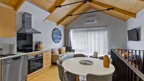 A modern kitchen with a built-in oven and dishwasher, a dining area with a round table and chairs, and a living space with a sofa and a TV mounted on the wall. - Central Queenstown Apt 15a - with Gym walk to town (Queenstown)