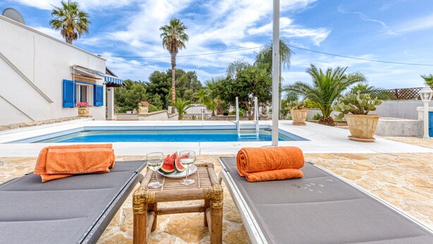A poolside area with two lounge chairs, a table with a watermelon and glasses, and a view of the pool and surrounding greenery. - Cozy house with pool 1km from sandy beach in Pescoluse (Pescoluse)