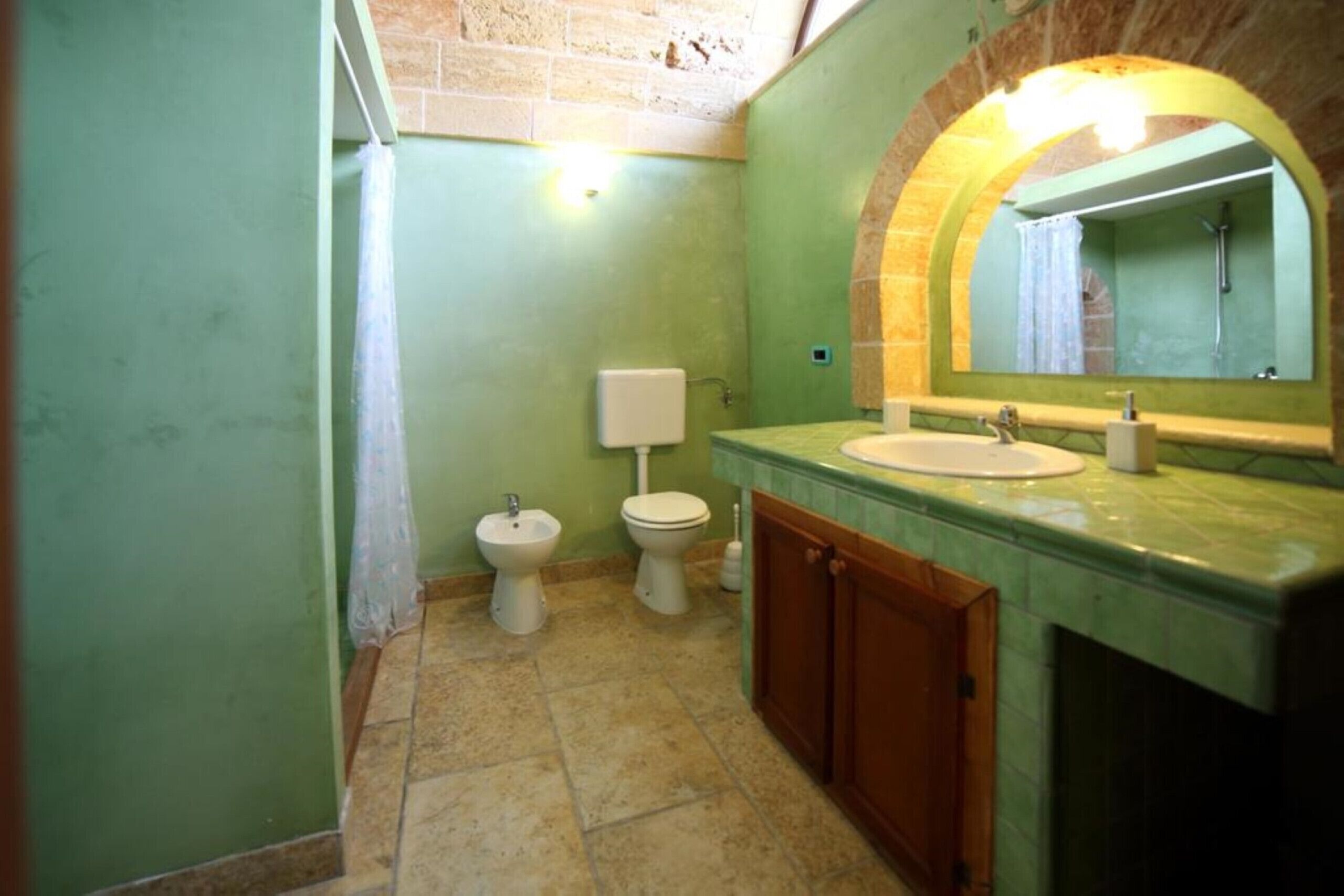 A bathroom with a green wall, a marble sink, a wooden cabinet, a bidet, and a toilet.