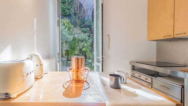 Cocina moderna con una olla de cobre en la encimera, una cafetera y vistas a un jardín por la puerta.
