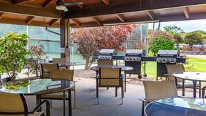 An outdoor patio with a covered seating area, a grill station, and a view of a tennis court.