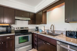 Una cocina moderna con armarios de madera oscura, electrodomésticos de acero inoxidable, un horno doble, microondas, cafetera y lavavajillas.