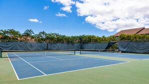 A tennis court with a net, surrounded by palm trees and a building in the background.