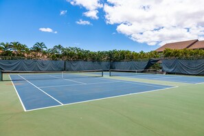 A tennis court with a net, surrounded by palm trees and a building in the background.