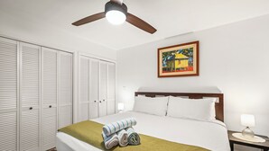 Habitació d'hotel amb llit, tauleta de nit, làmpada, ventilador de sostre i un quadre a la paret.