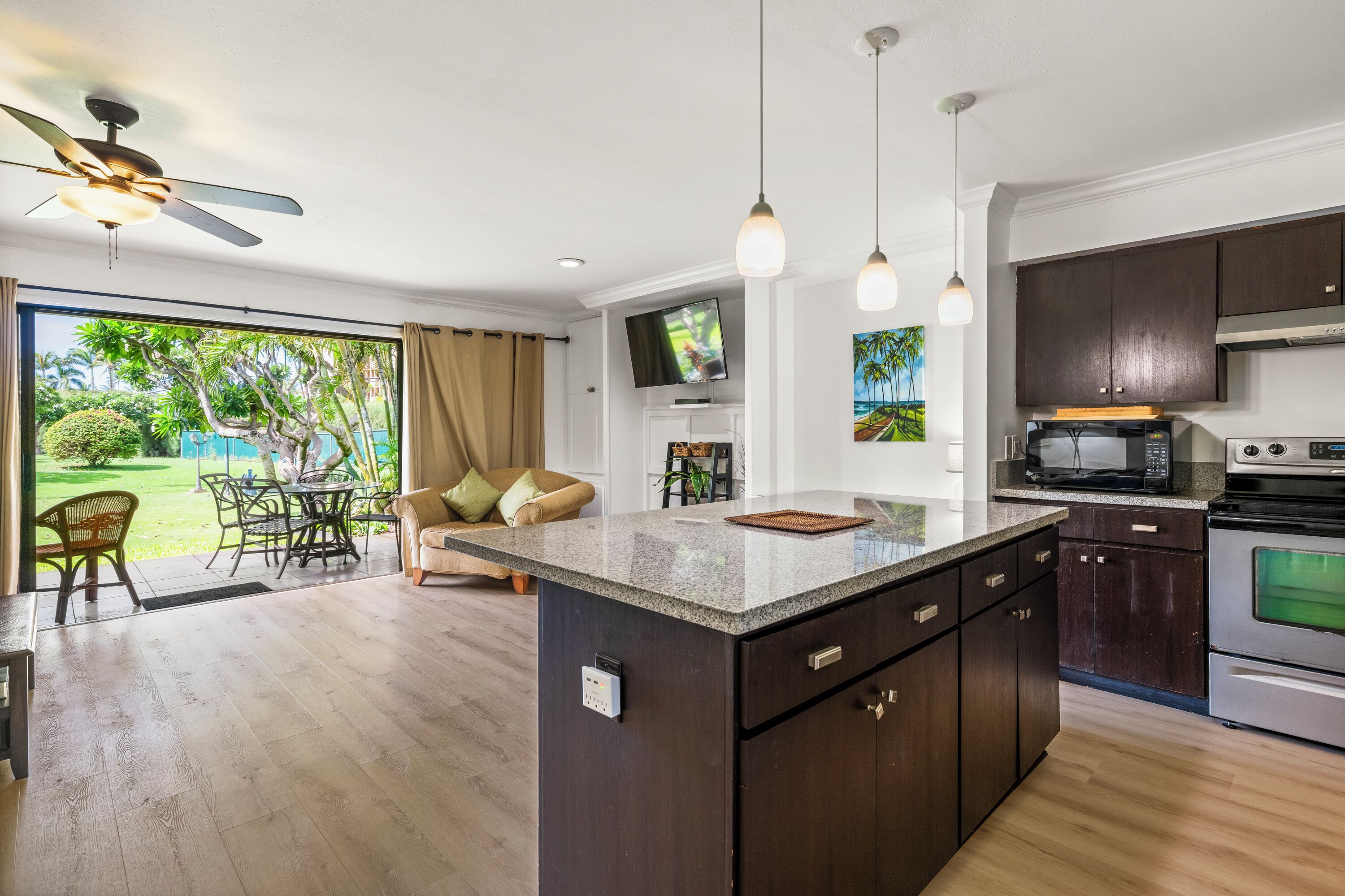 A modern kitchen with a central island, dark cabinetry, and a dining area with a view of a garden.