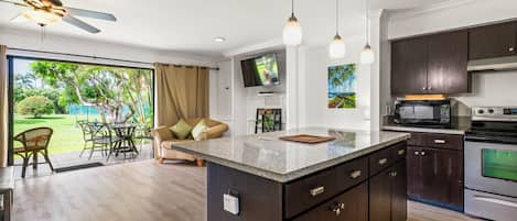 A modern kitchen with a central island, dark cabinetry, and a dining area with a view of a garden.