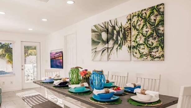 A dining area with a long table set for a meal, featuring decorative vases and a large floral painting on the wall. - Pickleball, Game Room, Heated Pool, 4 Min to Beach (Bradenton)