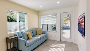 A living room with a blue sofa, two windows with blinds, a small table, and a door leading outside. - Pickleball, Game Room, Heated Pool, 4 Min to Beach (Bradenton)