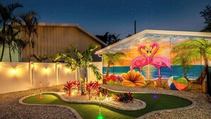 A landscaped garden with a pool, palm trees, and a mural of flamingos and beach scenery. - Pickleball, Game Room, Heated Pool, 4 Min to Beach (Bradenton)