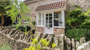 A stone building with a tiled roof, a window with a white frame, and a stone wall in front. - The Coach House (Ross-on-Wye)