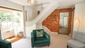 A spacious living room with a staircase, green and grey sofas, a brick wall, and a large window. - The Coach House (Ross-on-Wye)
