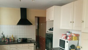 A kitchen with white cabinets, a black stove, and a microwave. There are various kitchen items on the counter. - L'hote 640 (Tarnos)