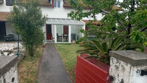 A pathway leading to a conservatory with a glass roof, surrounded by greenery and a red fence. - L'hote 640 (Tarnos)