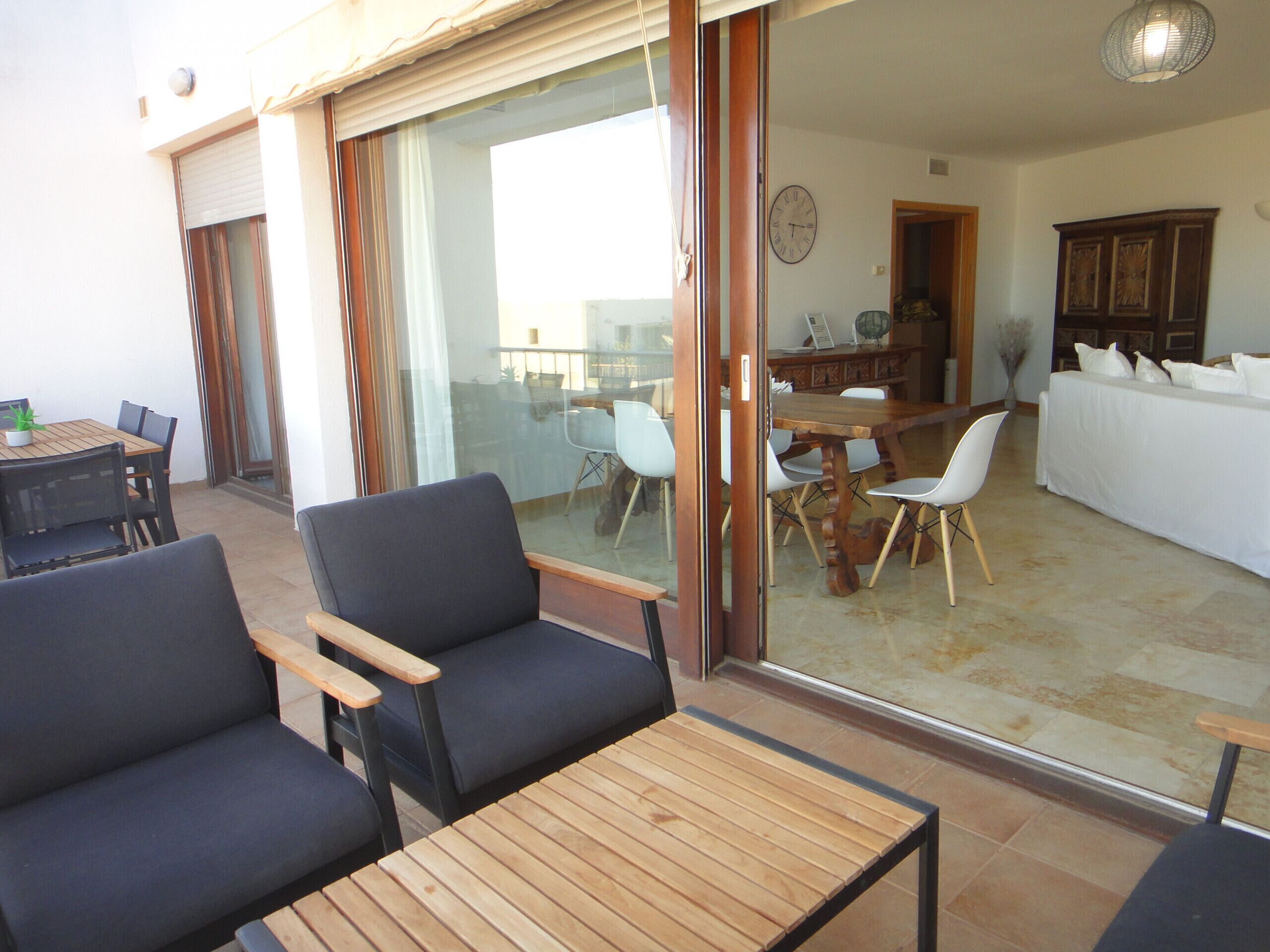 Ein Zimmer mit Holztisch und -stühlen, einer Couch und einer Schiebeglastür, die auf einen Balkon führt.