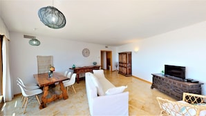 A spacious living area with a dining table, white chairs, a sofa, a television, and a decorative cabinet. - Lomas de los Monteros - Apartment with seaviews (Marbella)