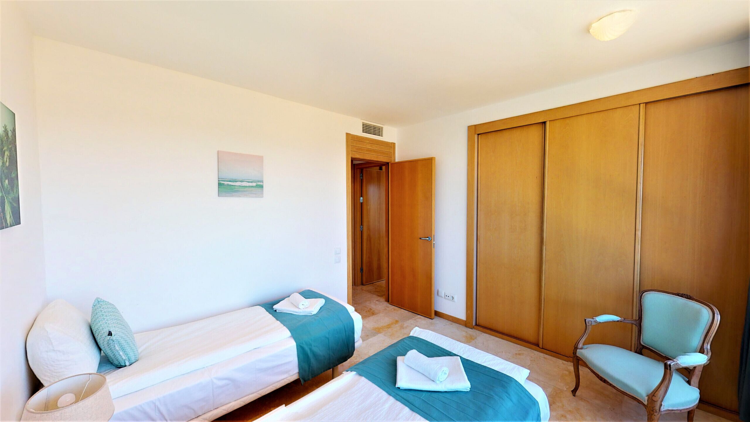 Une chambre d’hôtel avec deux lits simples, une armoire en bois, une chaise et un tableau au mur.