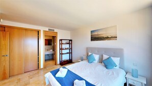 A hotel room with a bed, a nightstand, a bookshelf, and a bathroom visible through an open door. - Lomas de los Monteros - Apartment with seaviews (Marbella)