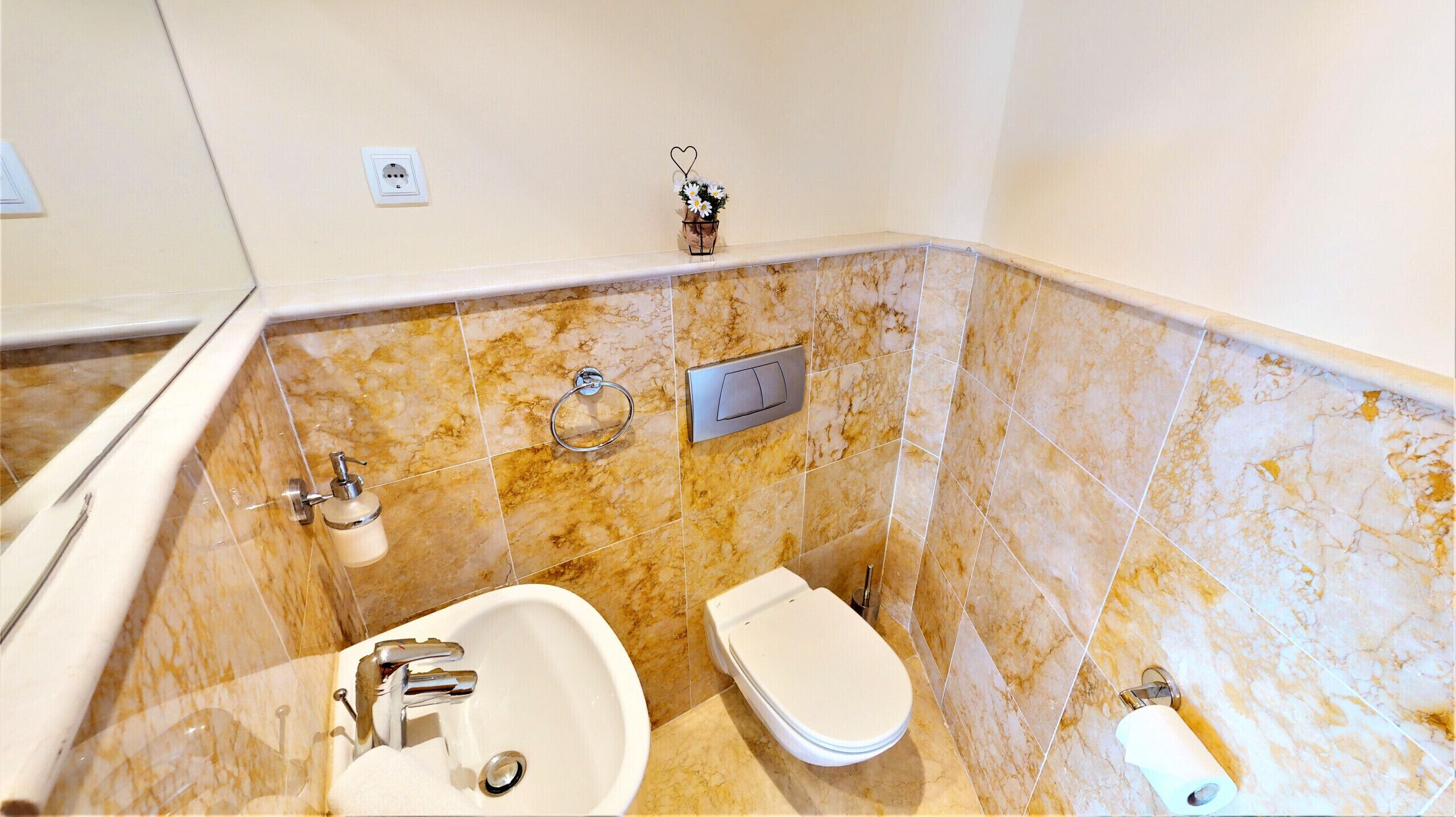 A bathroom with a marble-tiled wall, a sink, a toilet, and a towel dispenser.