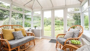 Un invernadero con muebles de mimbre, ventanas amplias y vistas al jardín.