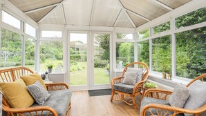 Un invernadero con muebles de mimbre, ventanas amplias y vistas a un jardín.