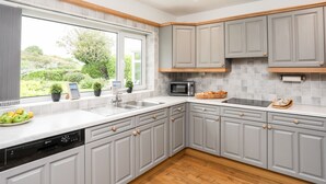 Una cocina moderna con armarios grises, microondas integrado y un ventanal con vistas a un jardín.