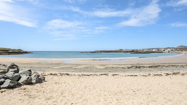 Una playa arenosa con rocas dispersas y un cielo azul despejado.