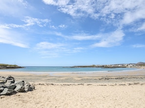 A sandy beach with scattered rocks and a clear blue sky. - Little Mead (Holyhead)