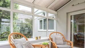 Una habitación acogedora con sillas de mimbre, una pequeña mesa con manzanas y ventanas amplias que dan a vistas de follaje.