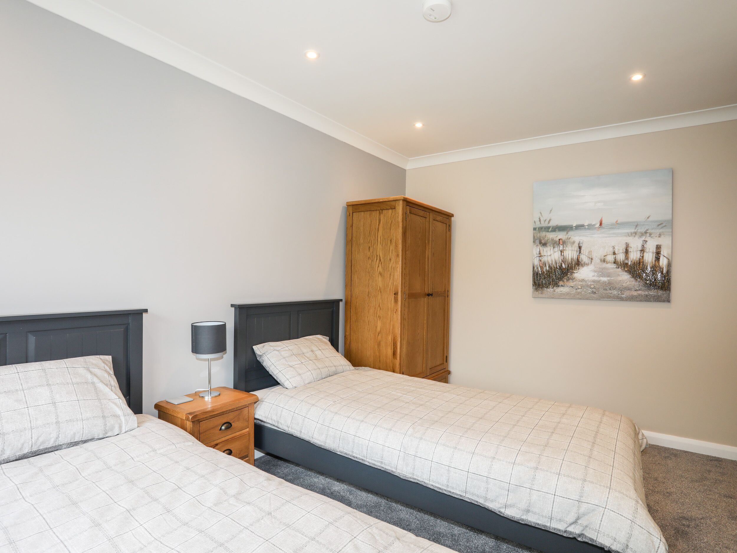 Een slaapkamer met twee bedden, een houten kledingkast, een nachtkastje met een lamp, en een schilderij aan de muur.